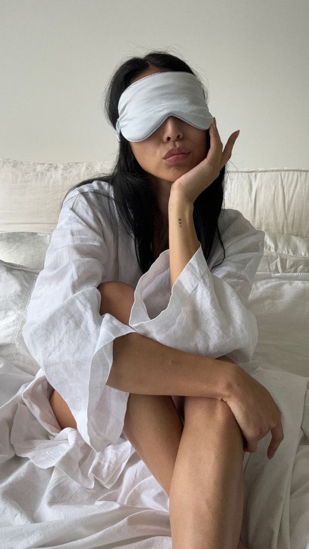 Vrouw draagt een zijden slaapmasker tijdens zitten op bed