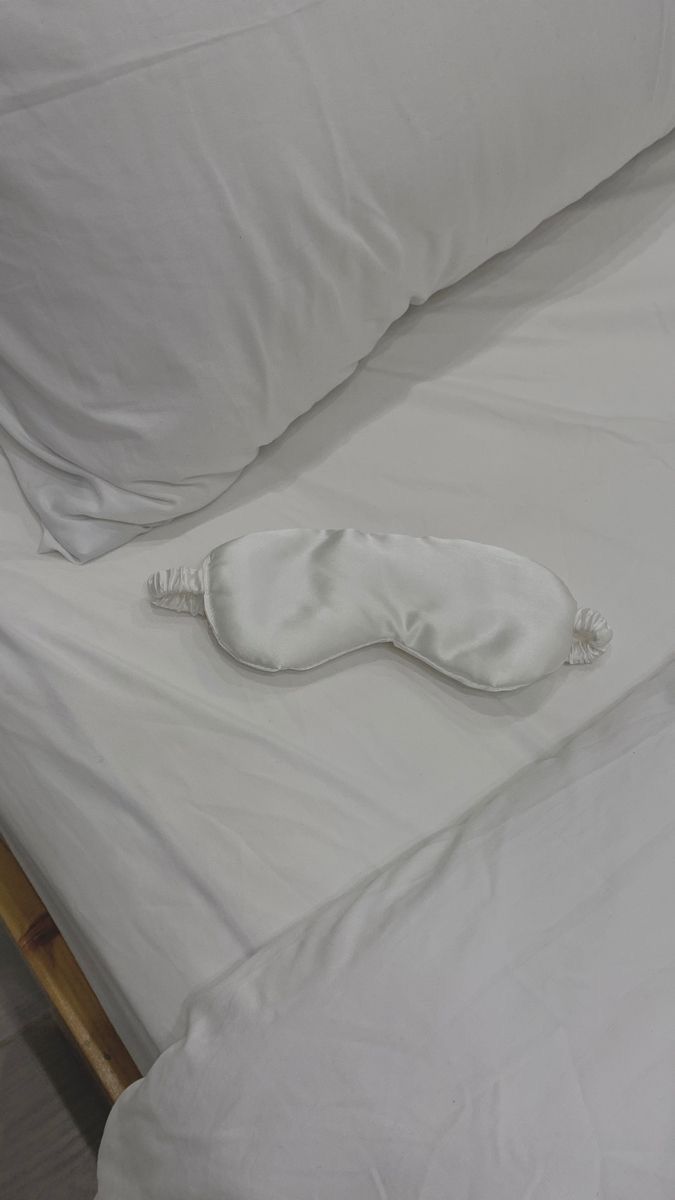 Zijden slaapmasker liggend op bed naast zijden kussen voor comfortabel slapen